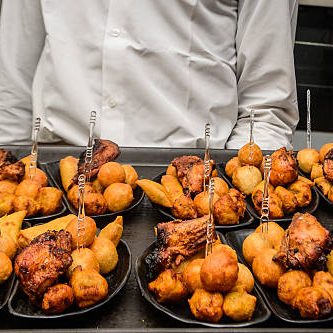 Server presenting assorted Nigerian small chops platter, featuring puff-puff, grilled chicken, samosas, and spring rolls at a social event in Lagos